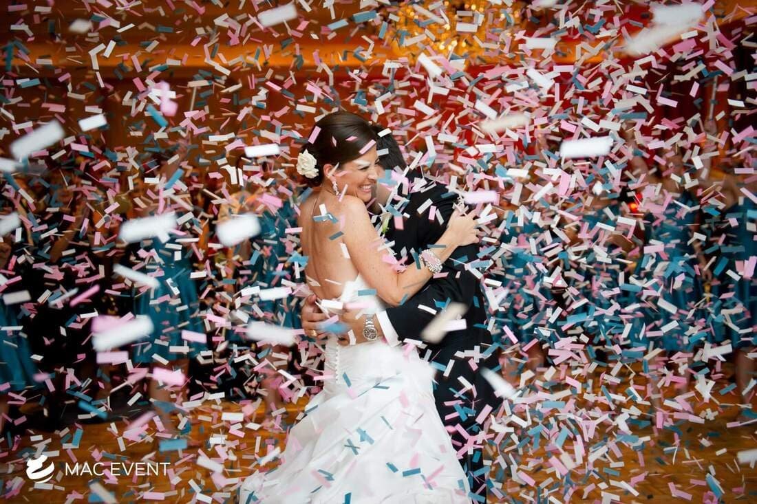 A bride and groom embrace joyfully during their wedding celebration, surrounded by a cascade of pink and blue confetti, creating a magical moment.